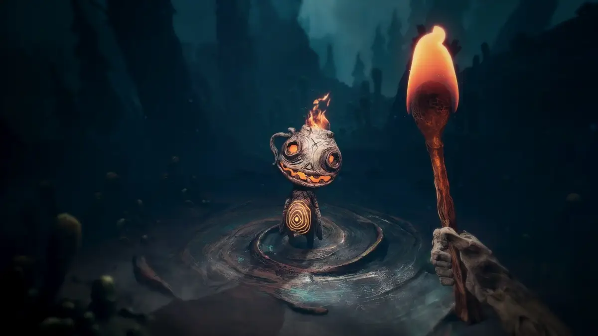 暗い異世界のような場所で、頭に炎を灯した不気味なクリーチャーが水たまりのような場所に立っています。画面右からは、誰かの手が持つ燃えるトーチが伸びています。