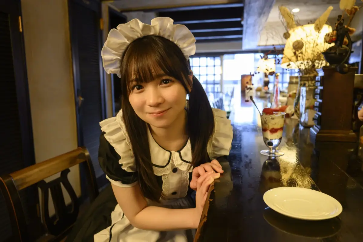 メイド服を着た若い日本人女性がカフェのカウンターで笑顔を見せています。