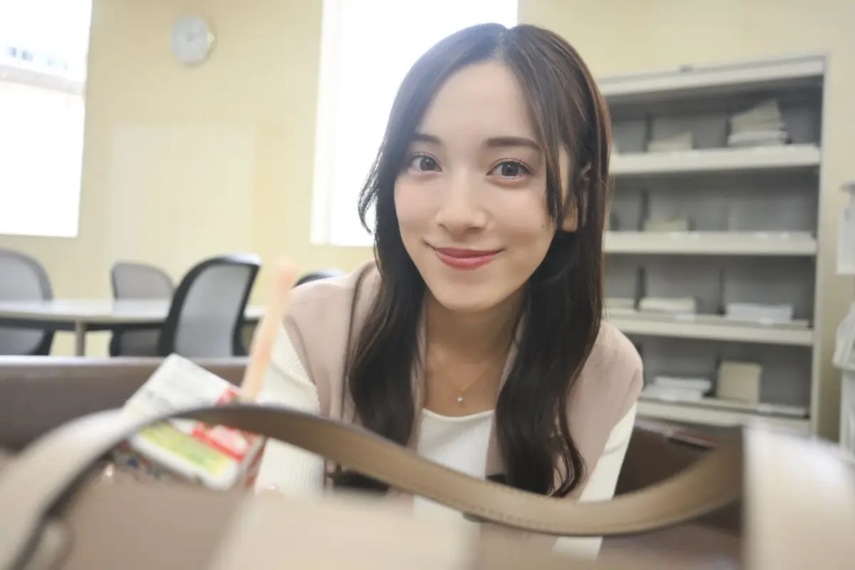 オフィスのような場所で、カメラに向かって優しく微笑む若い女性のポートレート。