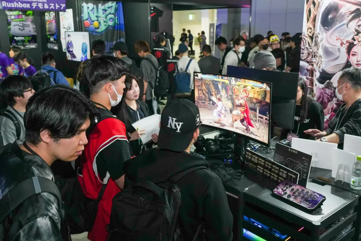 ゲームイベント会場で対戦型ビデオゲームのデモプレイを囲む人々